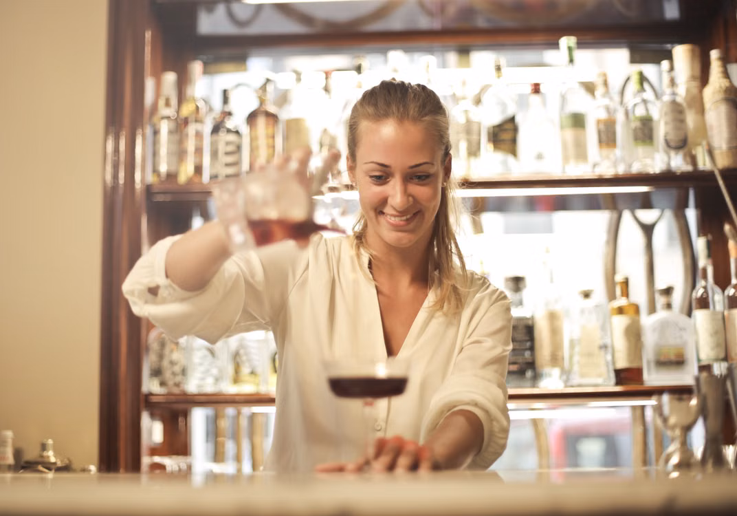 Illustrative photograph of a bartender pouring a drink into a stemmed glass.