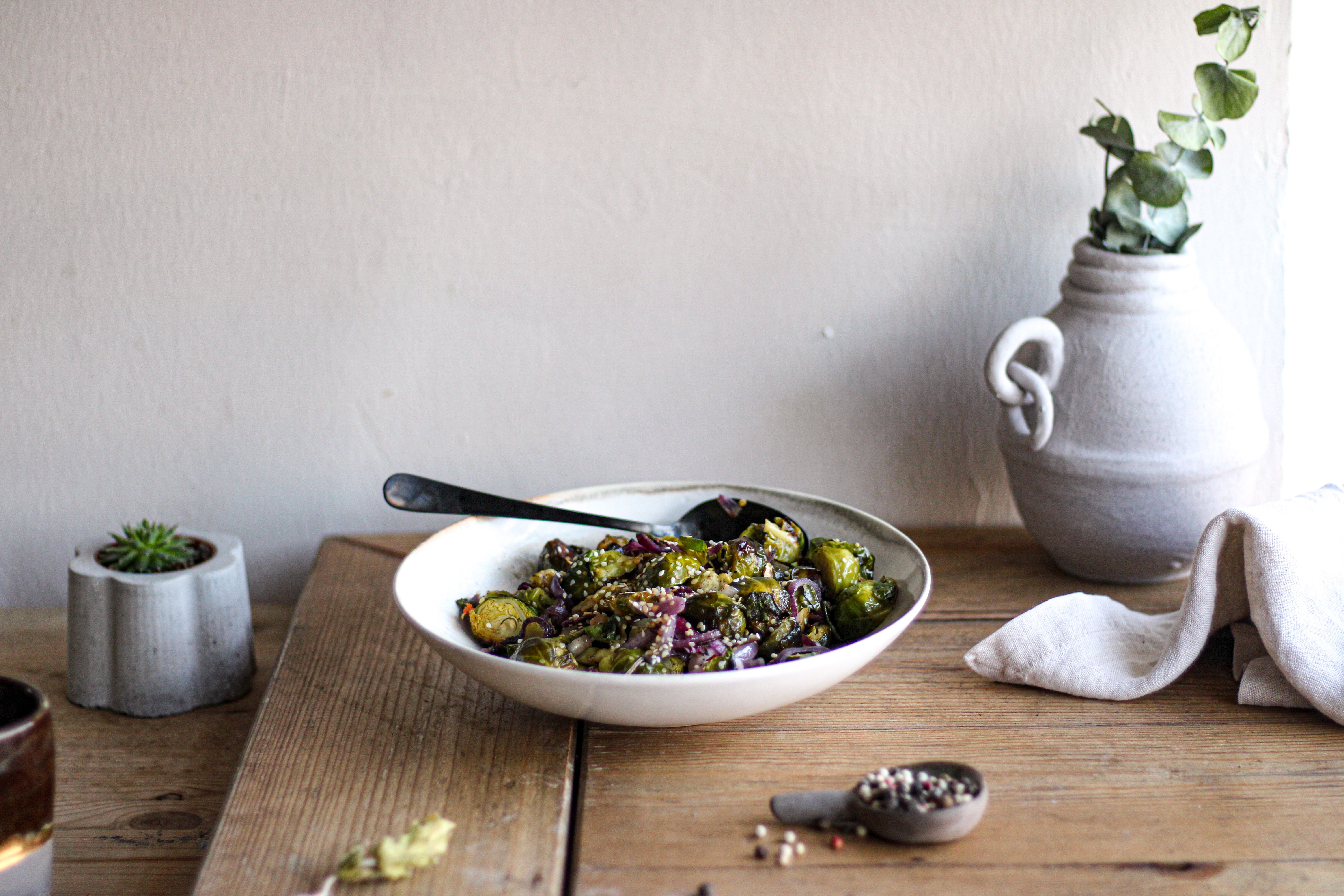 Roasted Brussels sprouts with seeds in a bowl beside a vase.