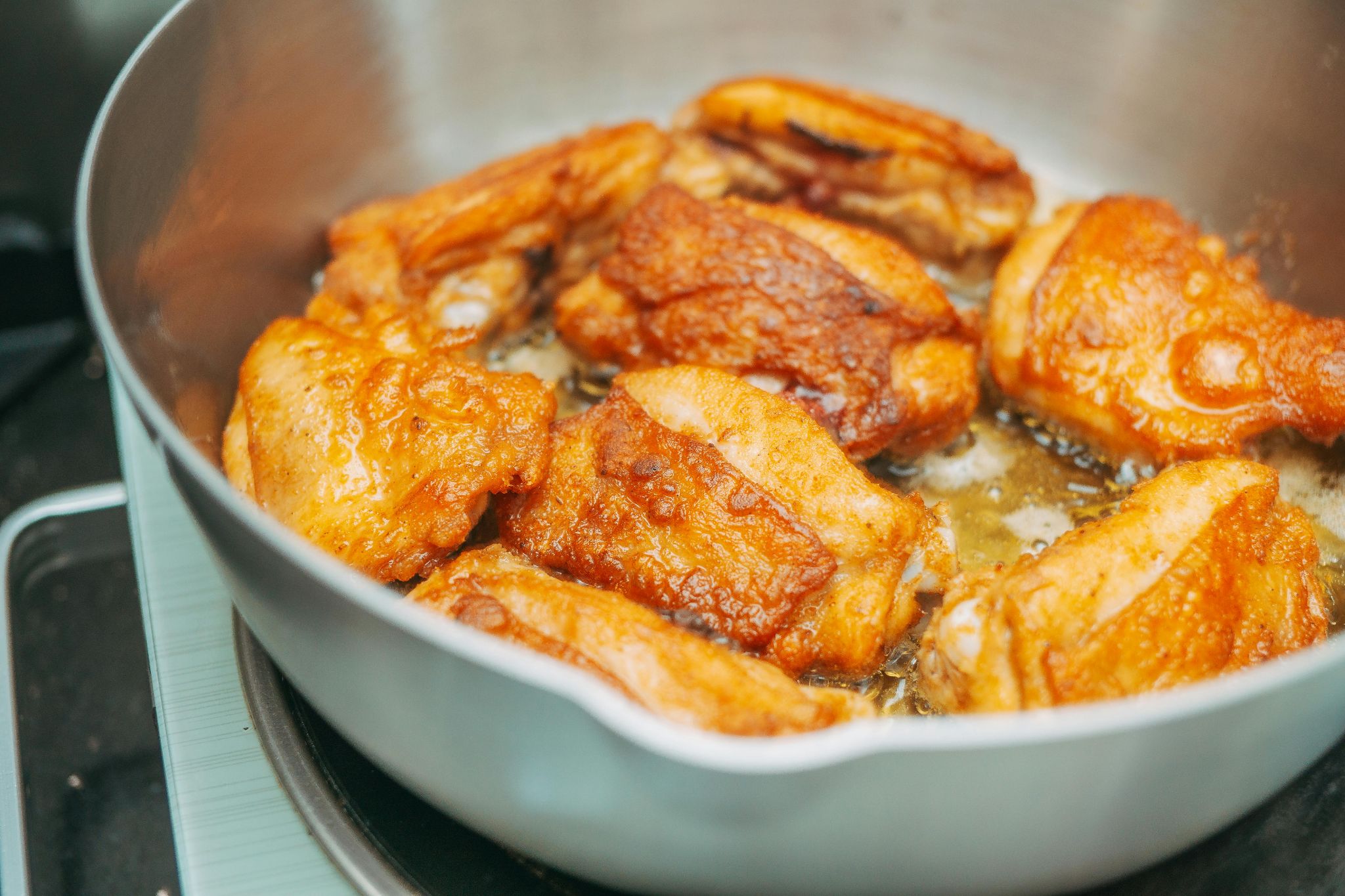 Chicken pieces frying in a pan.