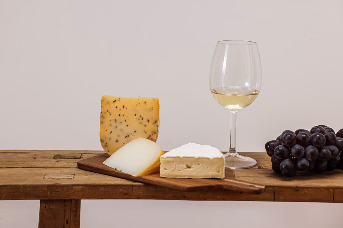 A glass of white wine beside cheeses and grapes on a wooden table.