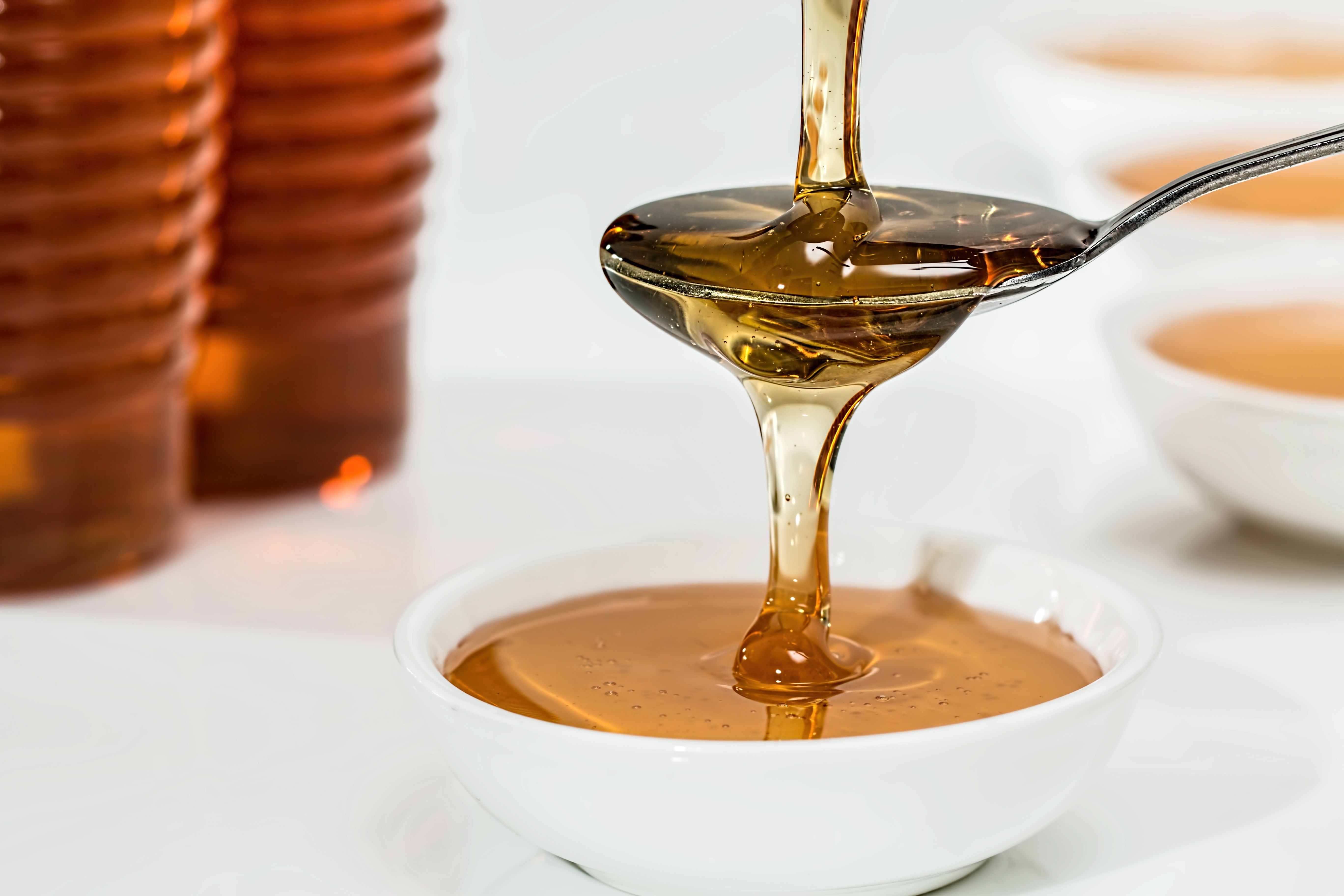 Honey dripping from a spoon into a white bowl.
