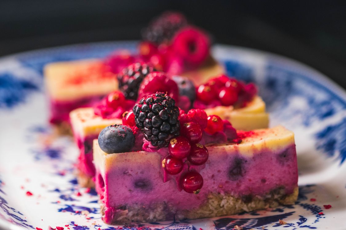 Slices of berry cheesecake topped with fresh berries on a patterned plate.