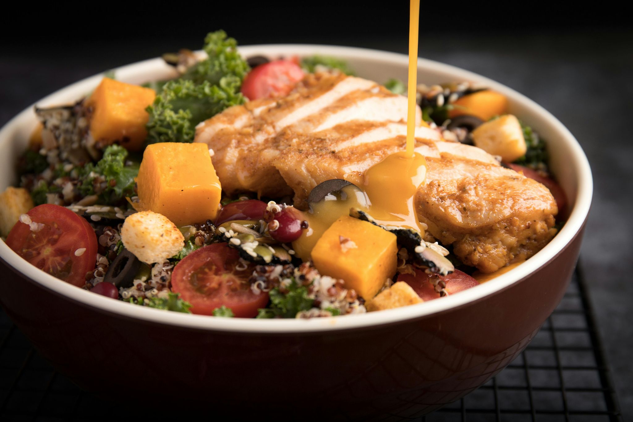 Sauce being poured over sliced chicken and vegetables in a bowl.