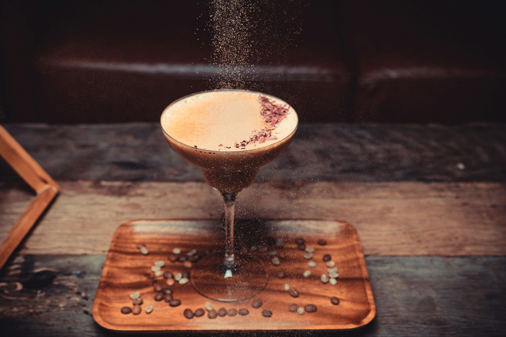 A dark drink with pale foam in a stemmed glass, with coffee beans on the tray.