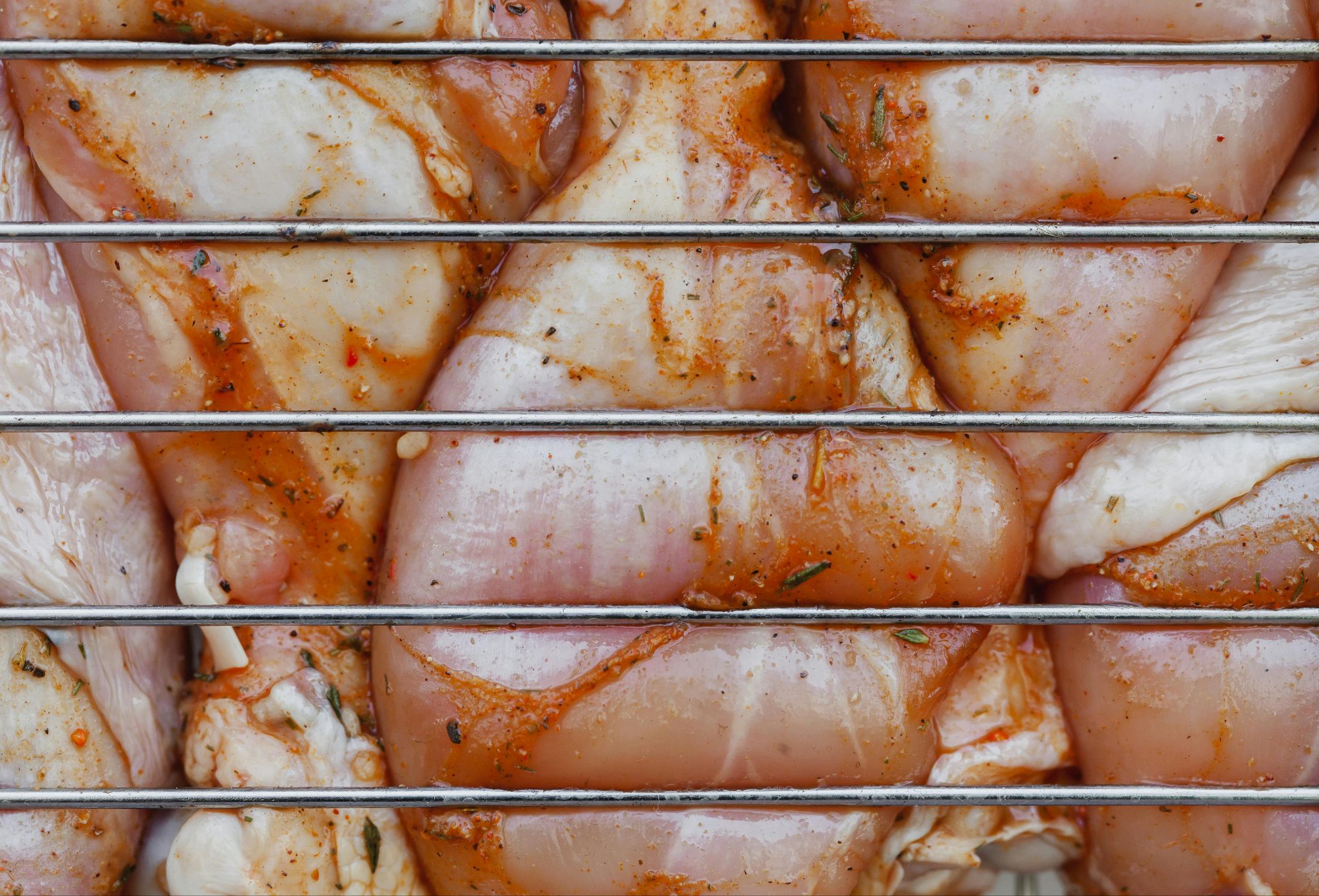 Seasoned chicken pieces behind a metal rack.