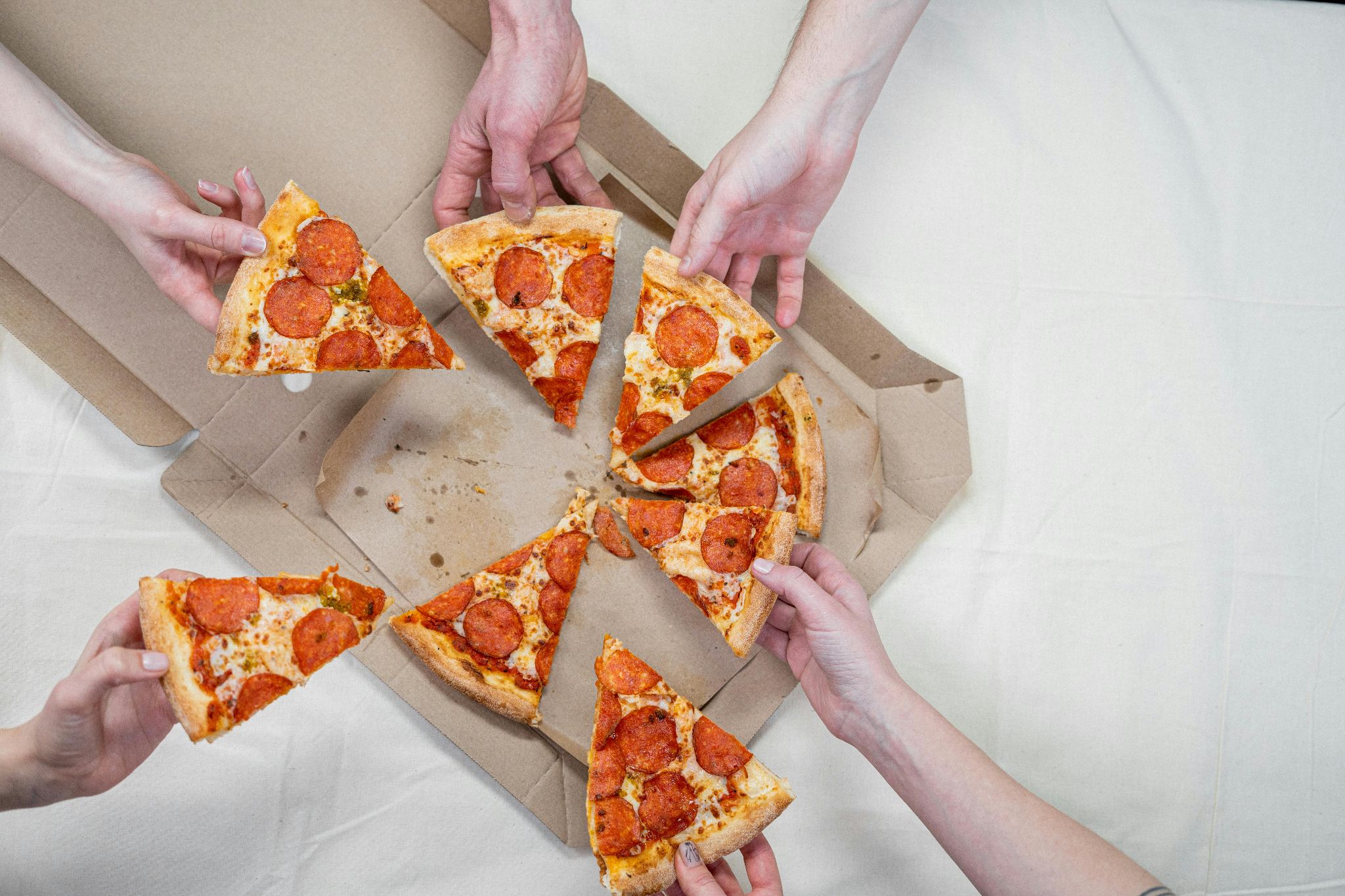 Hands taking pepperoni pizza slices from an open cardboard box.