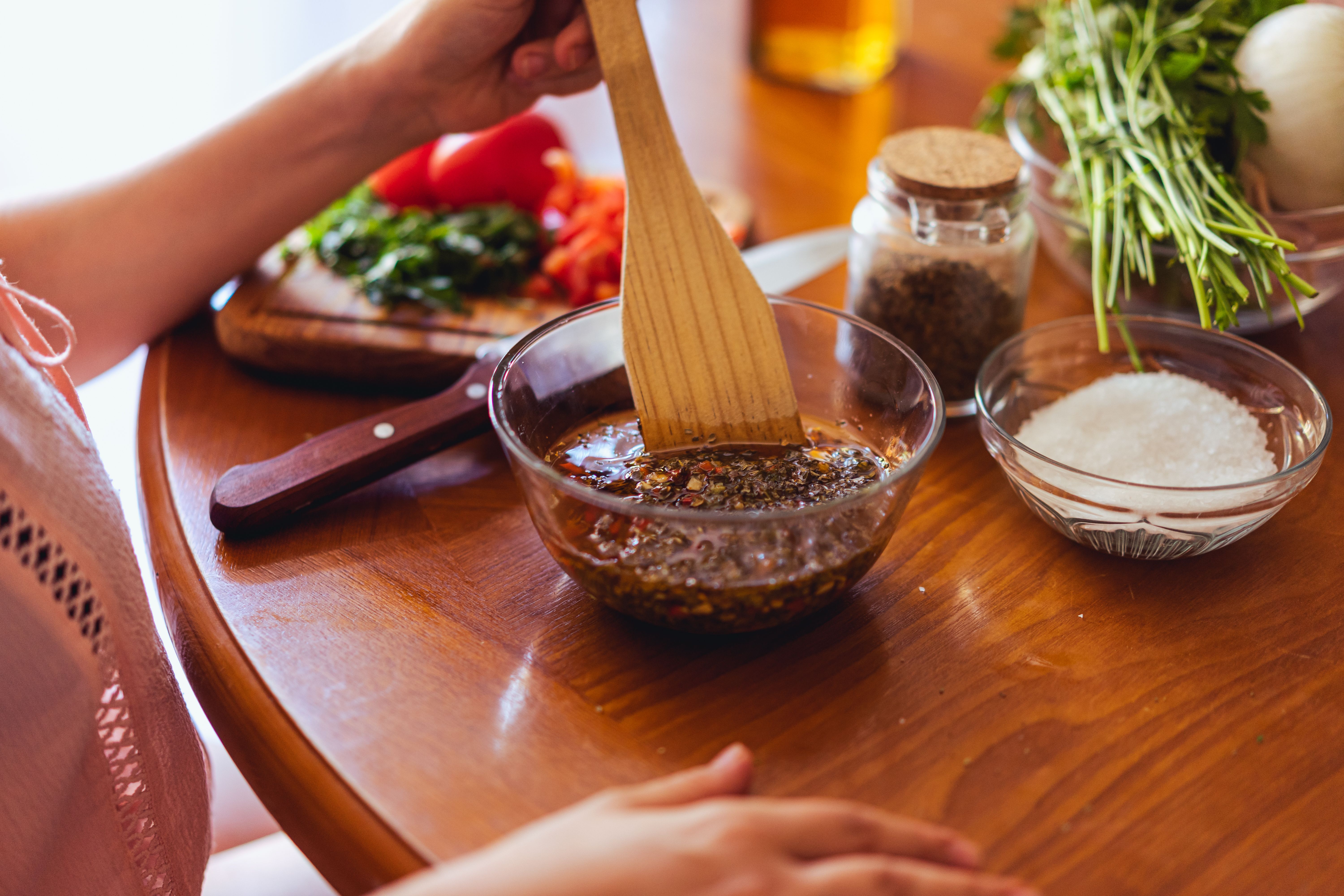 Hand mixing chimichurri in a glass bowl.