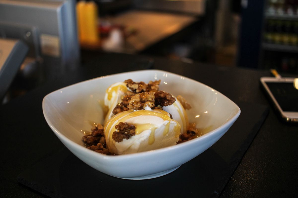 Ice cream with walnuts and a golden drizzle in a white bowl.