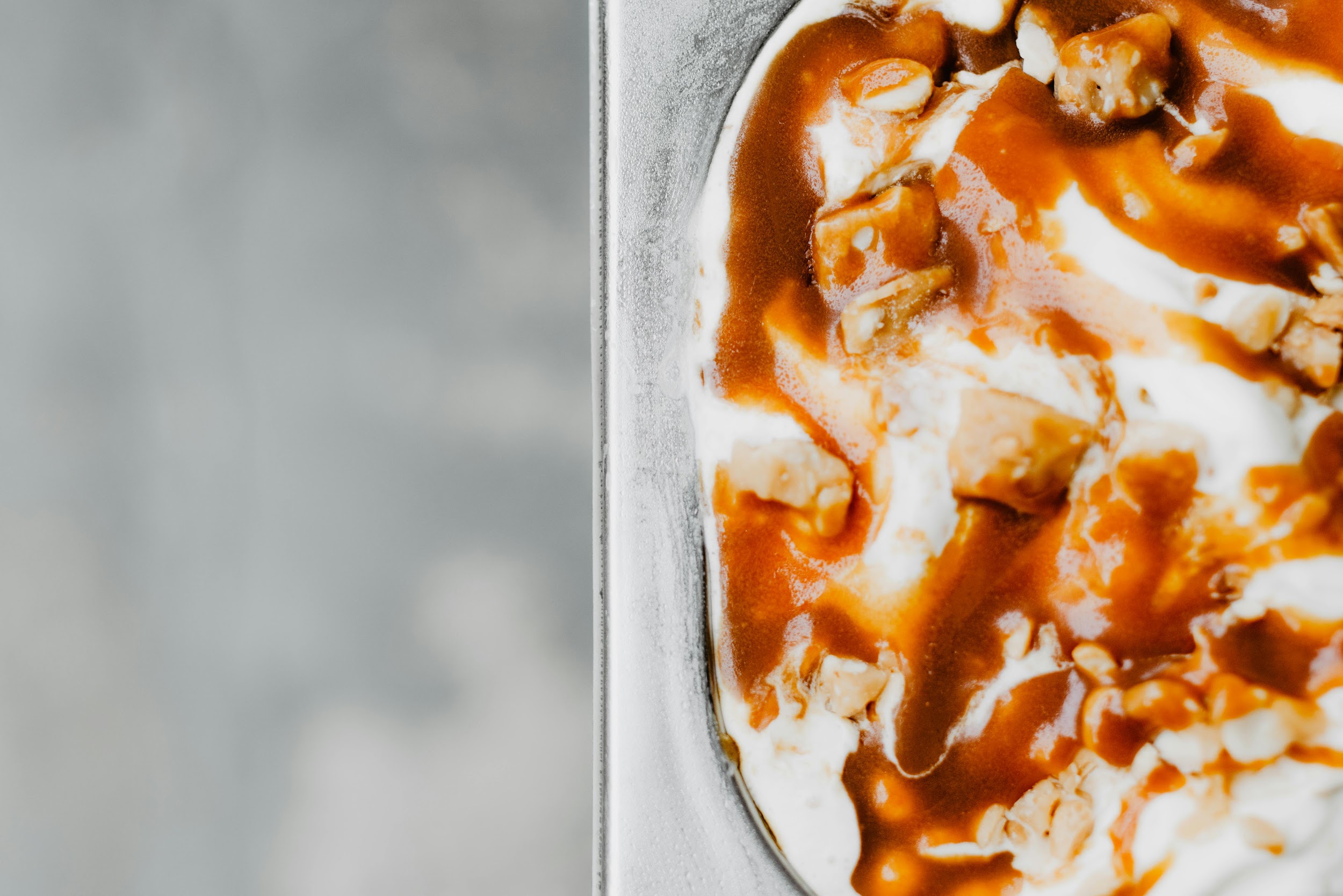 Ice cream with brown sauce and topping pieces in a metal tray.