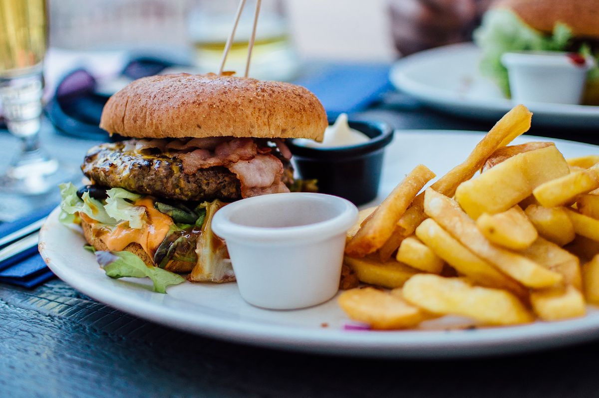 A burger with lettuce and cheese beside thick-cut fries and dipping bowls.