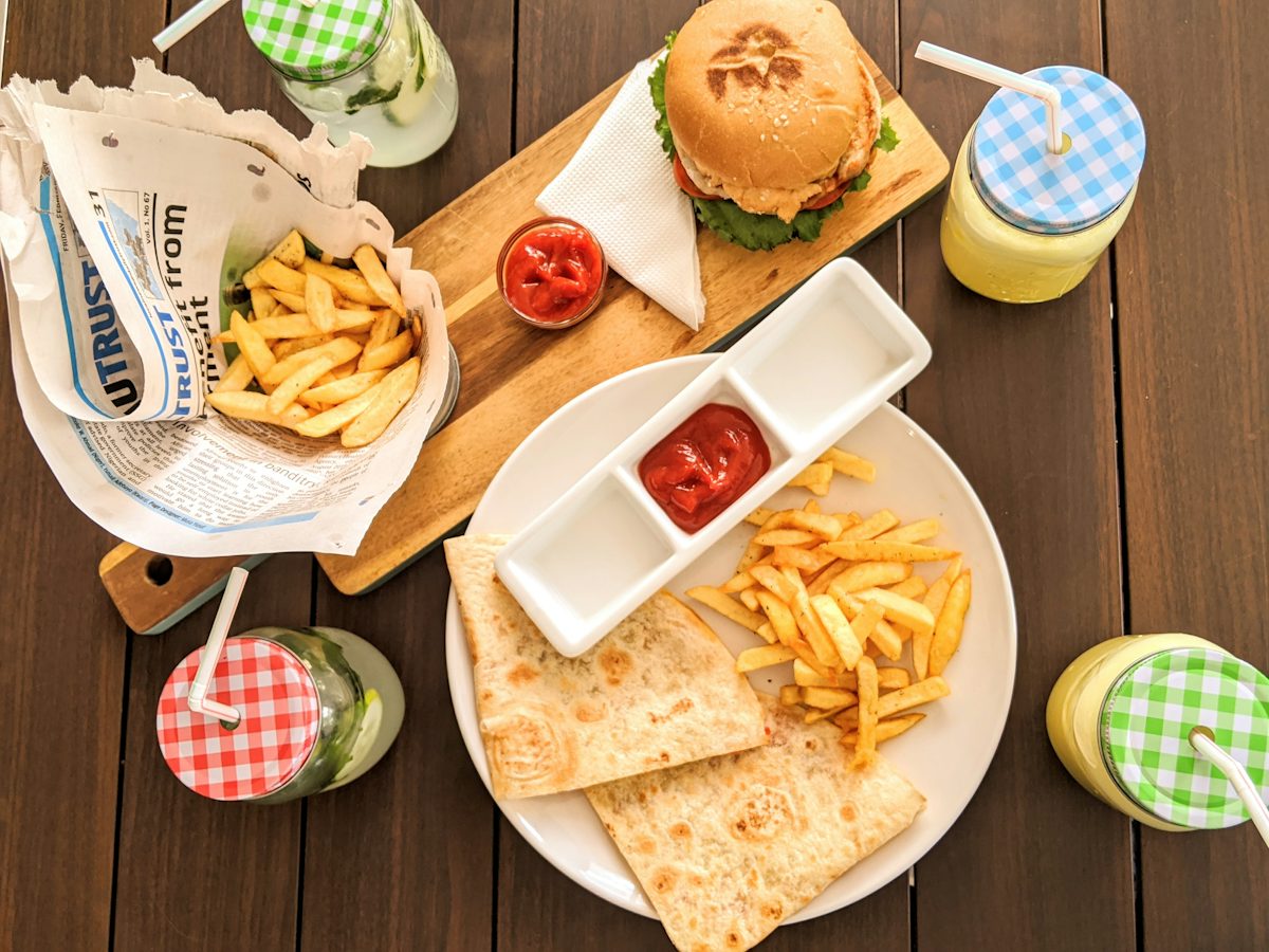An overhead view of a burger, fries, flatbread, sauces and drinks on a wooden table.
