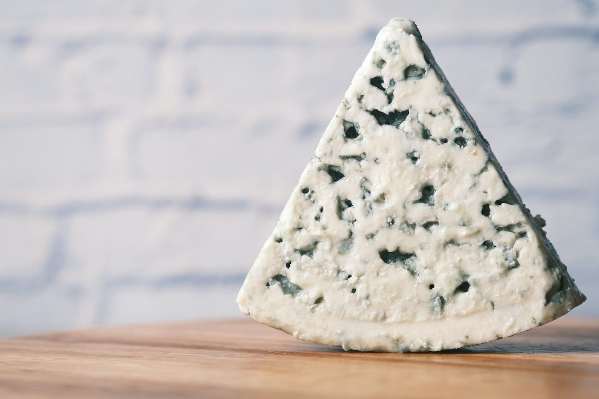 A wedge of blue-veined cheese on a wooden surface.