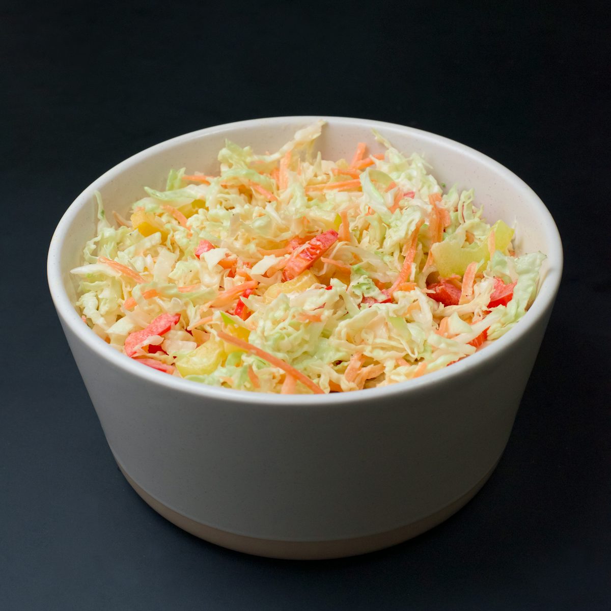 Shredded vegetable slaw in a white bowl against a dark background.
