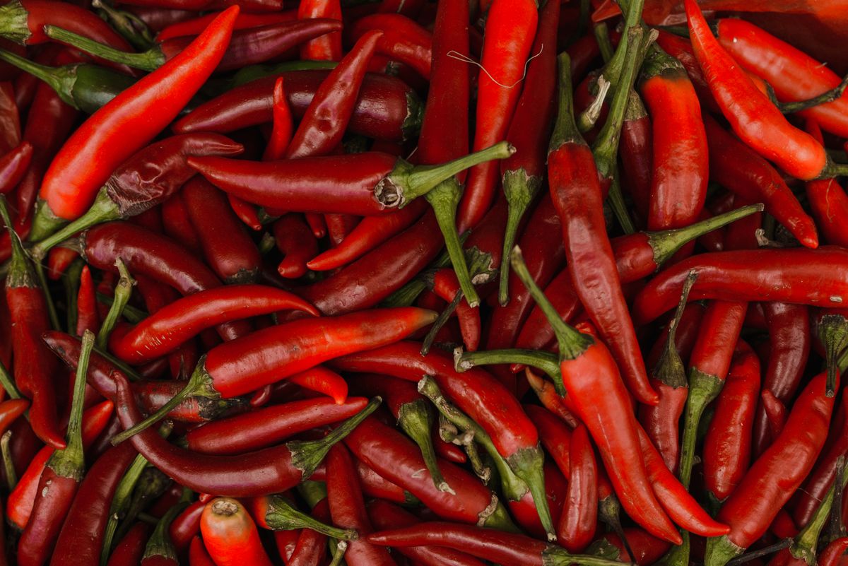 A close-up pile of red chili peppers with green stems.