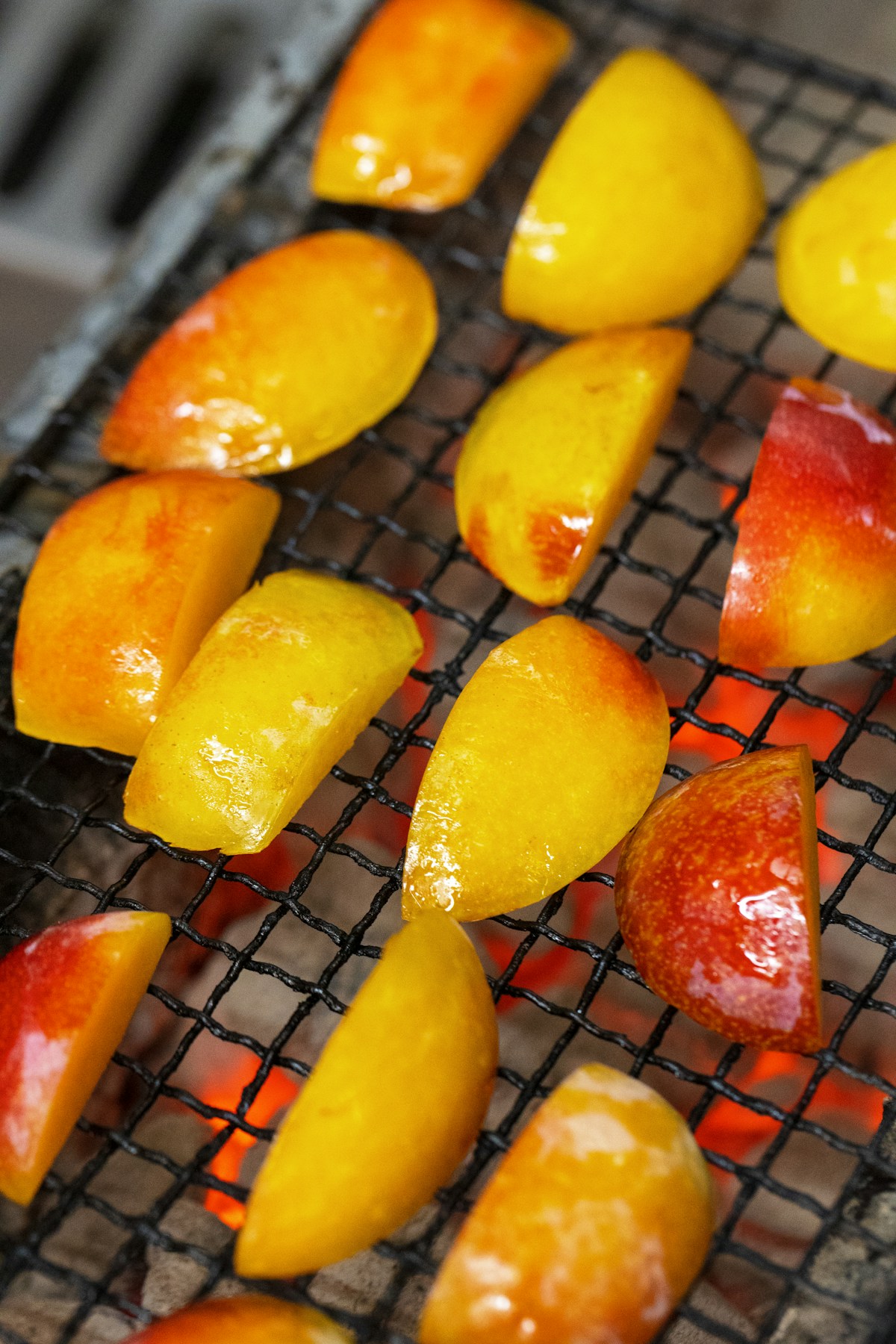 Yellow and red-skinned fruit pieces on a grill grate above glowing coals.