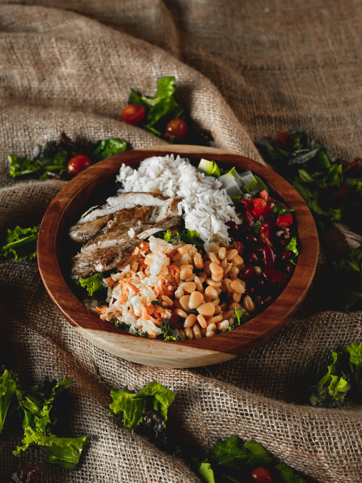 Sliced cooked chicken, white rice, corn, beans and salad arranged in a wooden bowl.