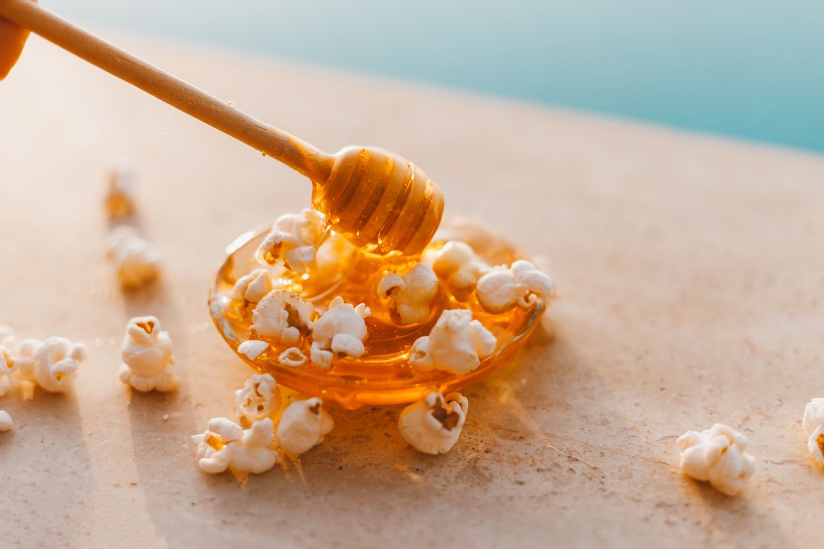 Honey and popcorn beneath a wooden honey dipper.