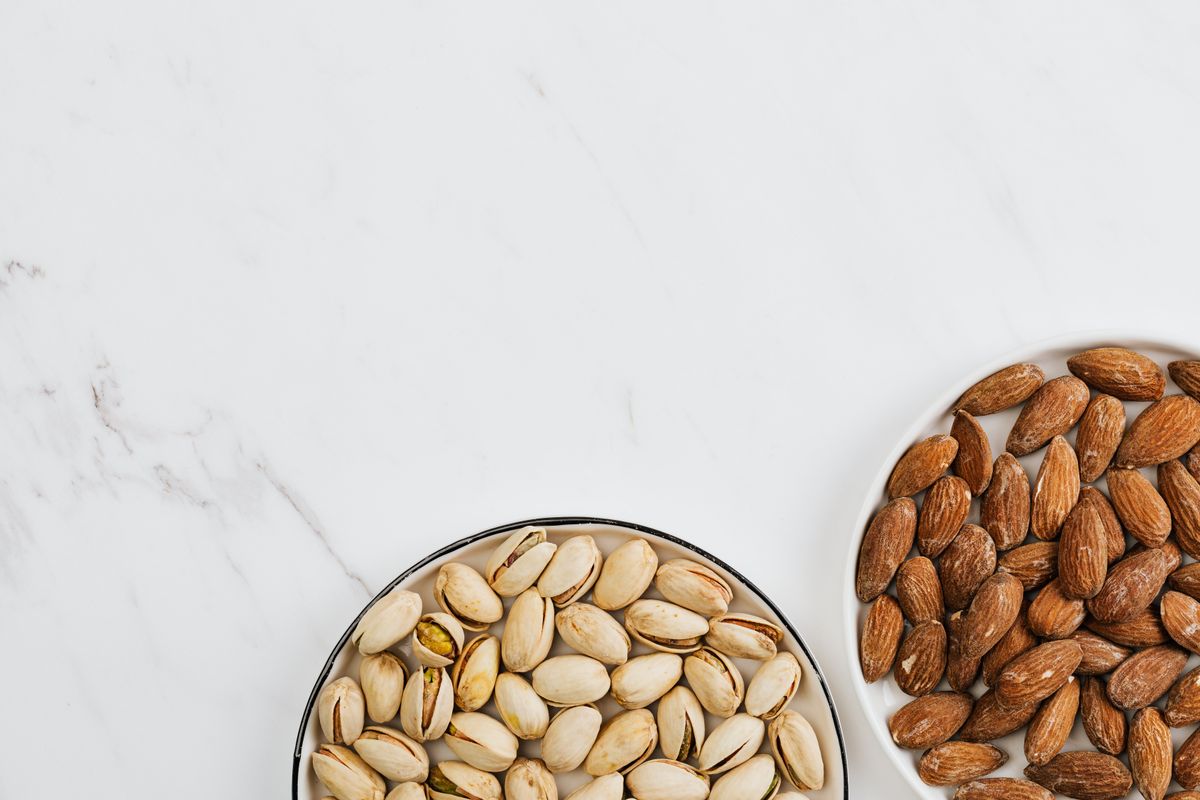 Almonds and pistachios in dishes on a white surface.