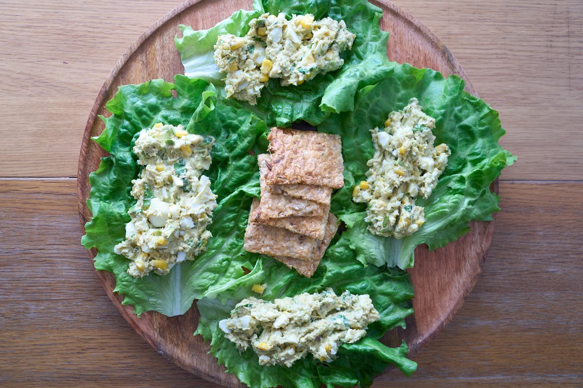 Lettuce leaves topped with a pale chopped filling around crackers on a round wooden platter.
