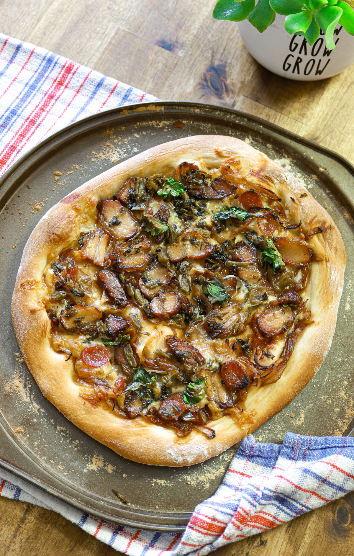 Pizza with browned toppings and leafy greens on a metal tray.