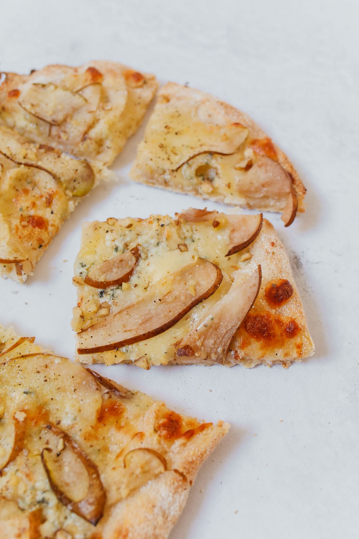 Pear slices and melted cheese on pizza pieces arranged on white paper.