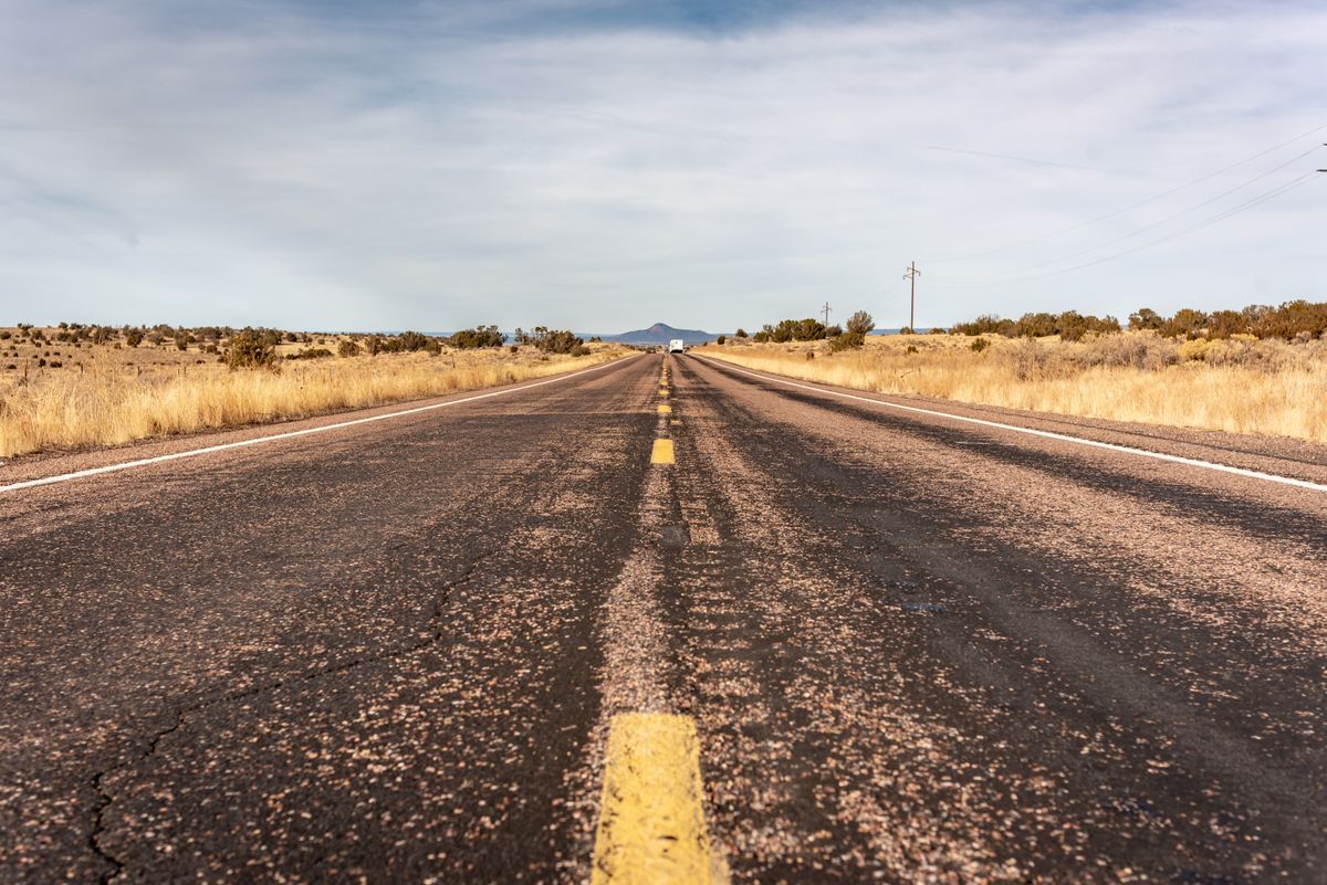 A straight two-lane road crosses dry grassland beneath a cloudy sky.