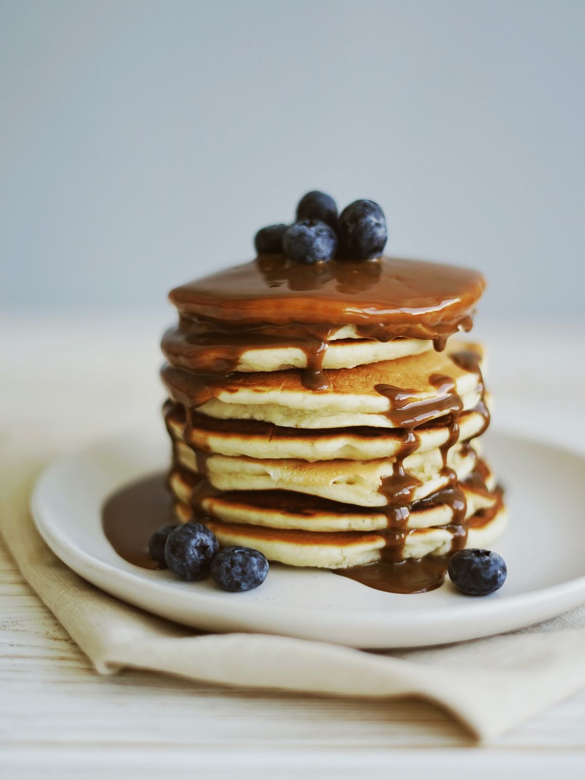A stack of pancakes topped with blueberries and a glossy brown topping on a white plate.