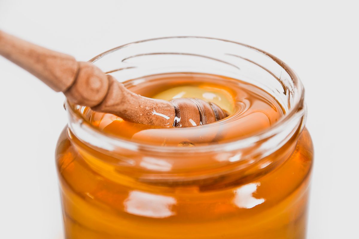 A wooden honey dipper resting in an open glass jar of amber honey.