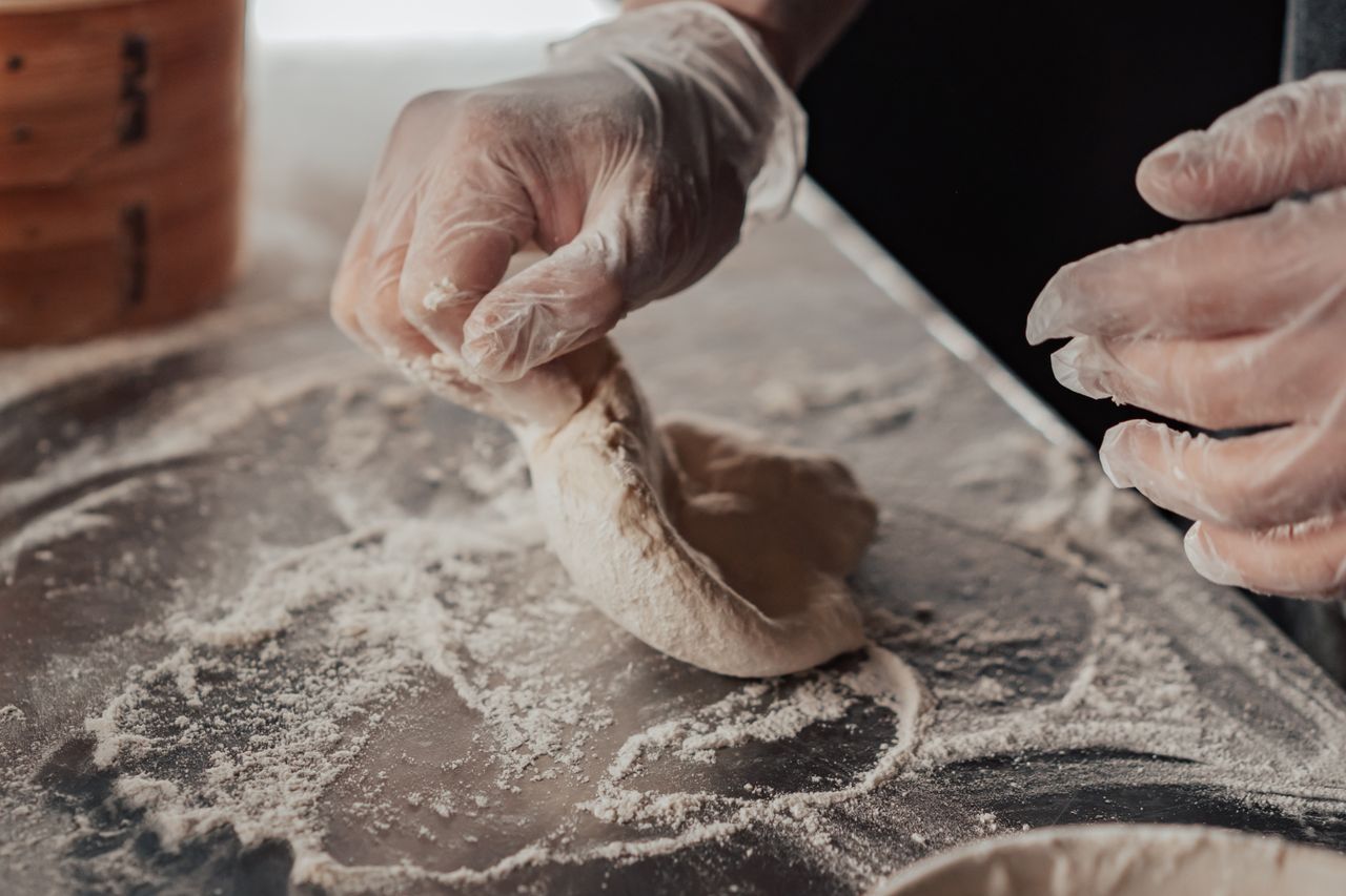 Gloved hands folding dough on a flour-covered counter.