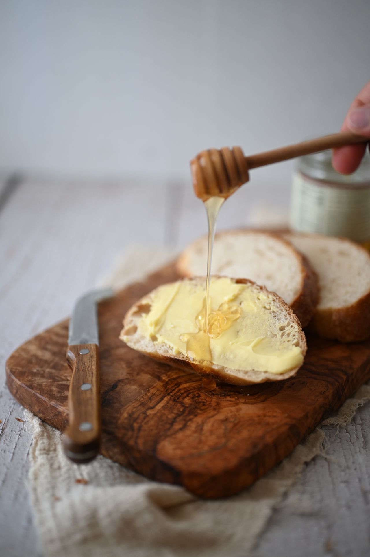 Honey dripping from a wooden dipper onto buttered bread on a wooden board.