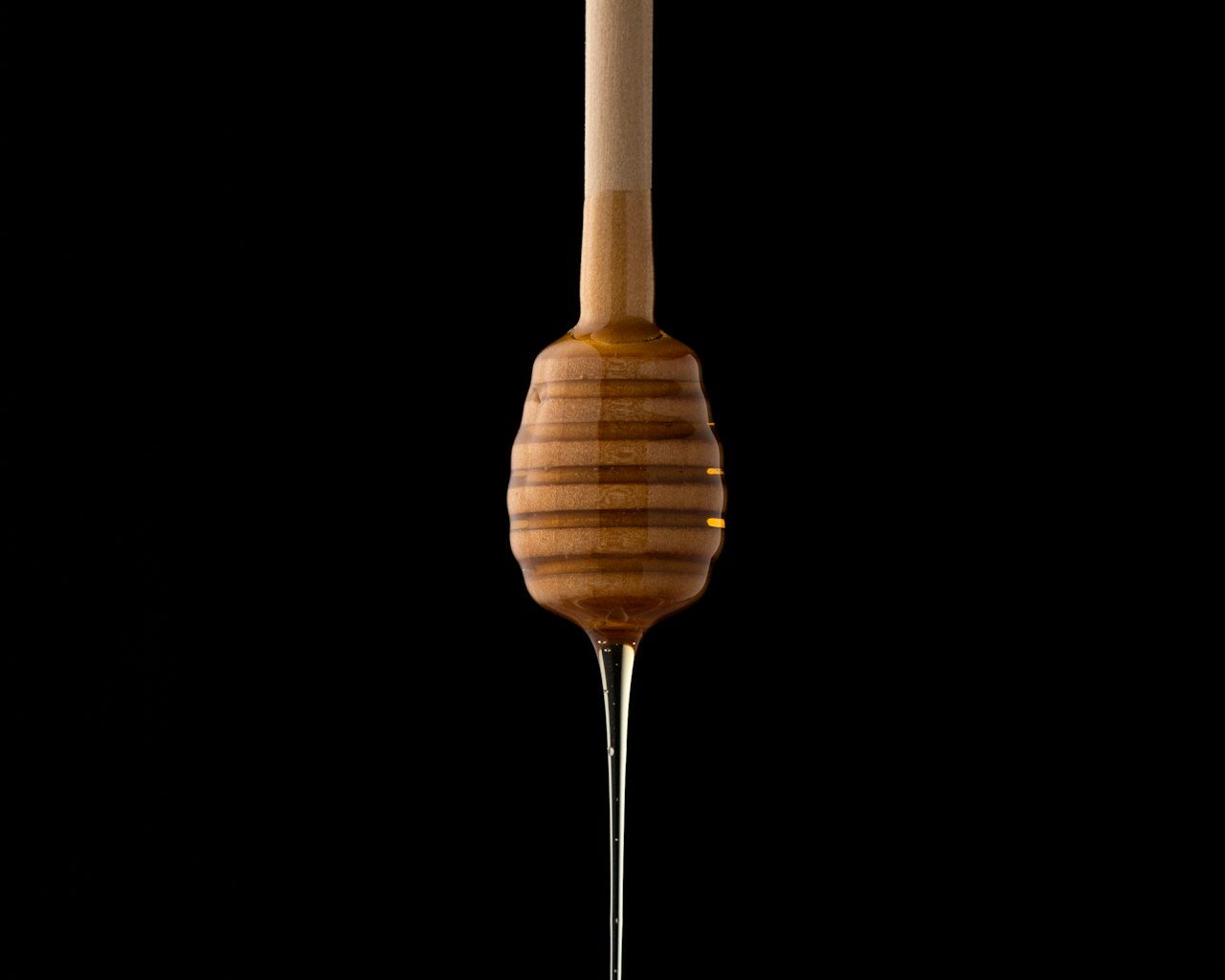 Honey drips from a wooden dipper against a black background.