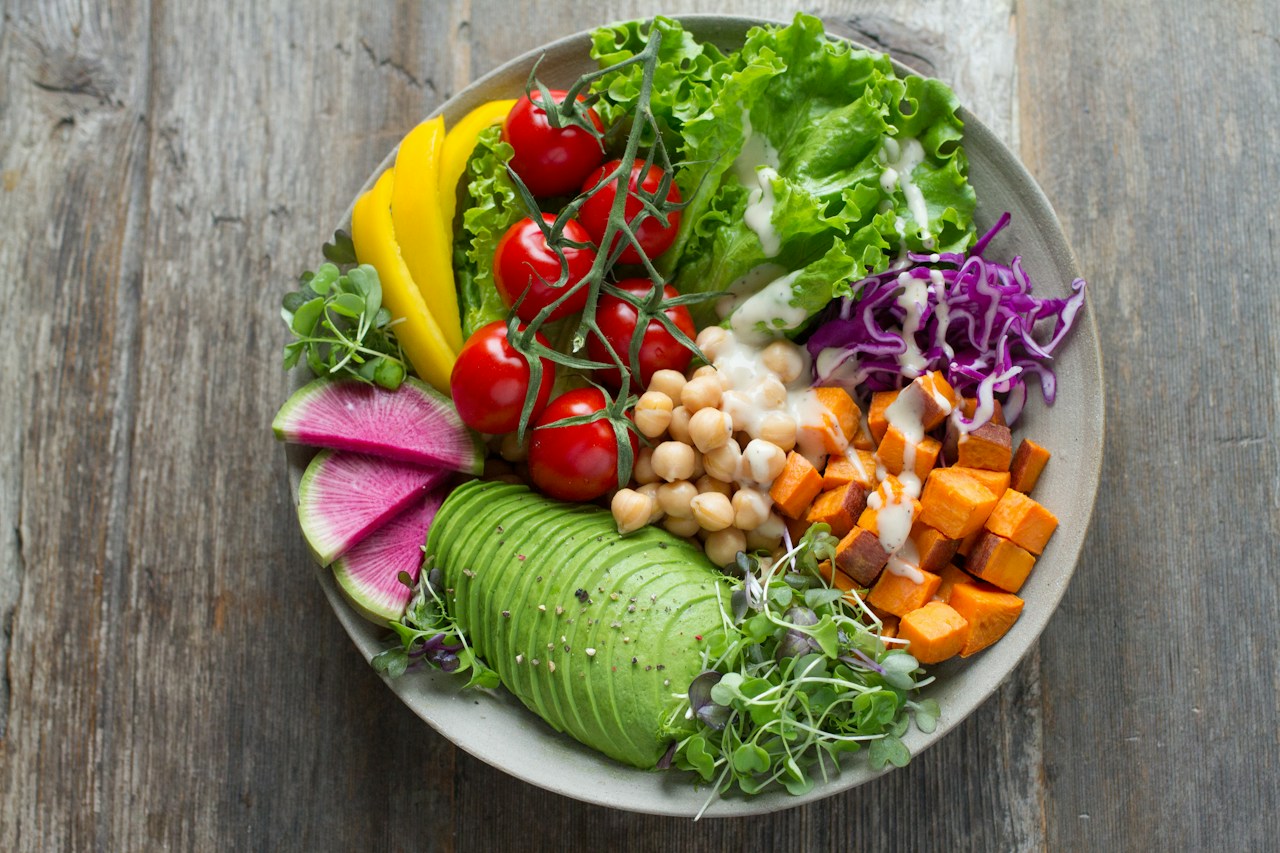 A bowl holds lettuce, avocado, tomatoes, chickpeas and other vegetables with a pale dressing.