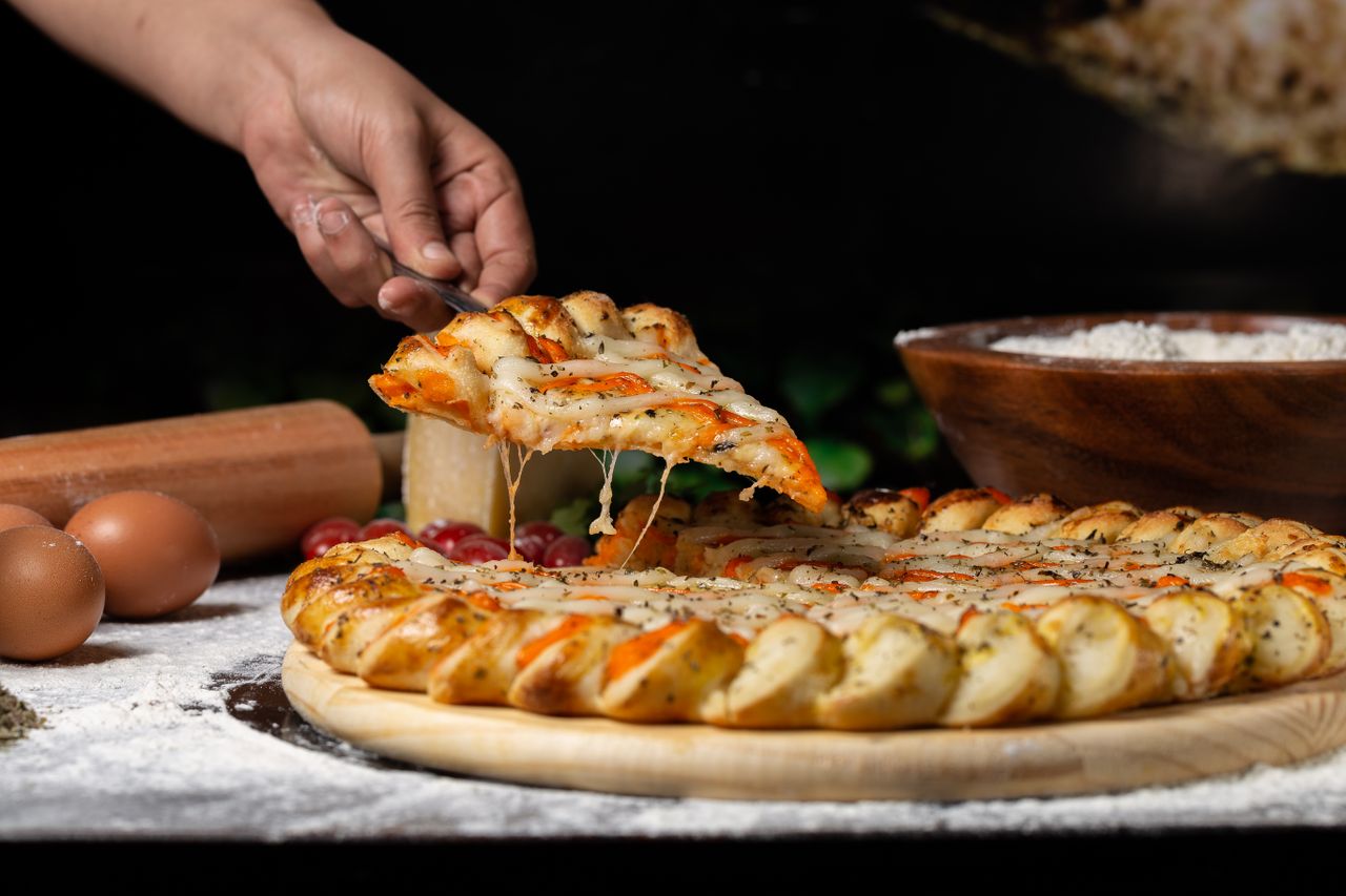 A hand lifts a cheese-covered pizza slice from a wooden board.