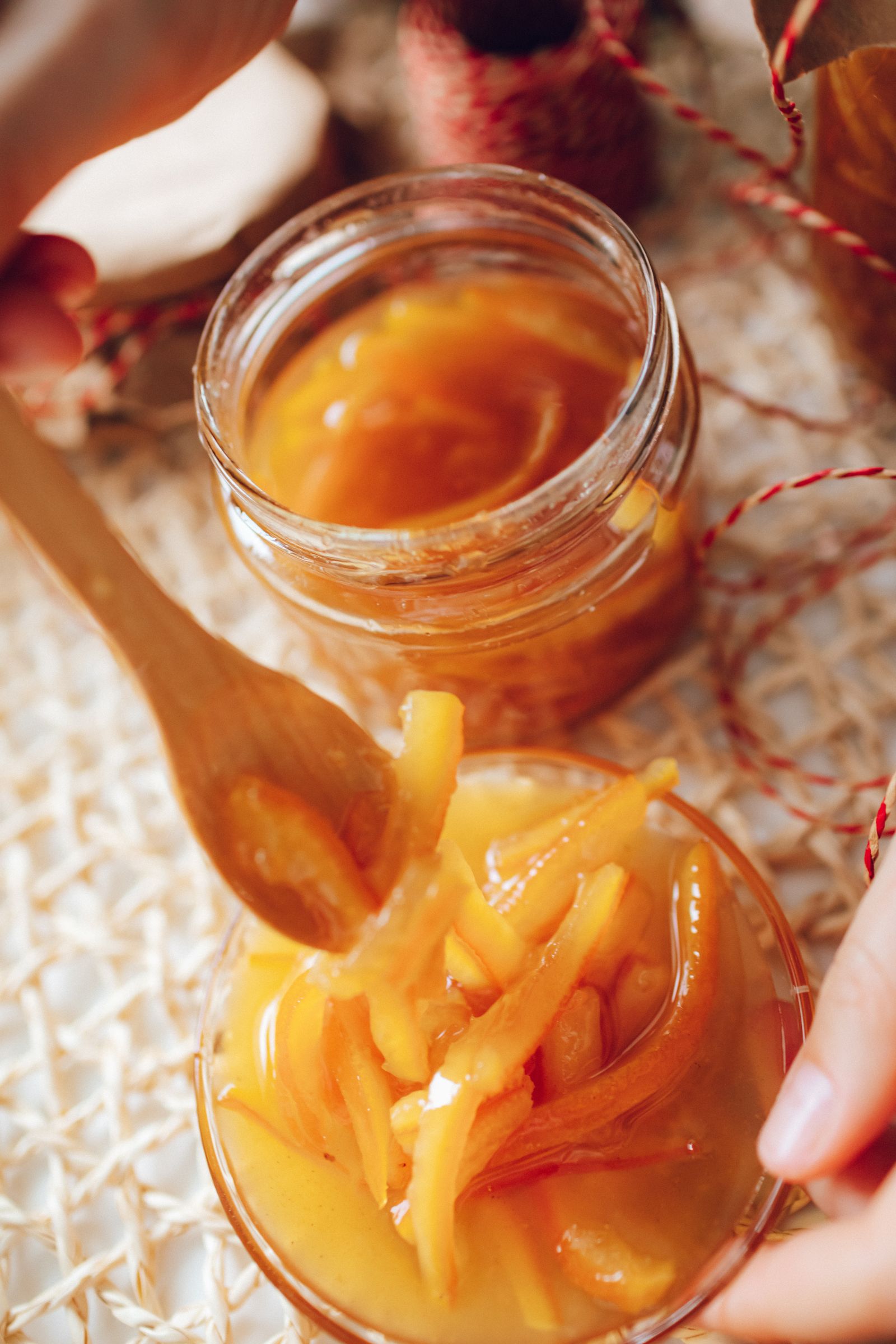 A wooden spoon holds orange peel preserves beside an open glass jar.