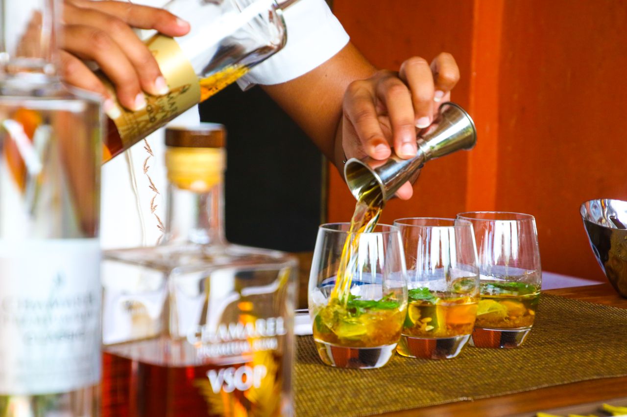 A bartender pours amber liquid from a jigger into short glasses with green leaves.