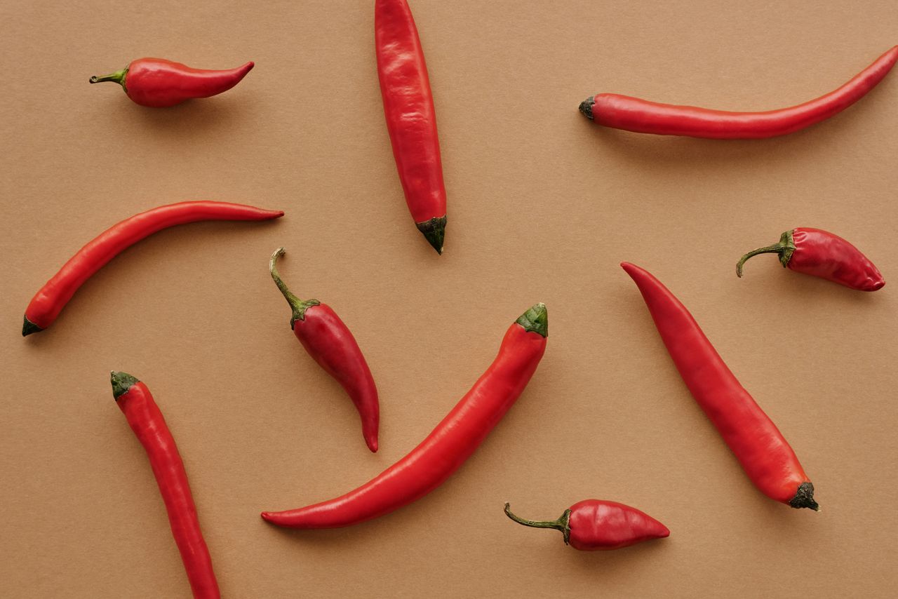 Red chili peppers lie on a tan textured surface.