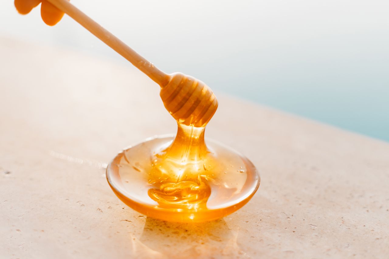 Honey runs from a wooden dipper into a shallow glass dish.