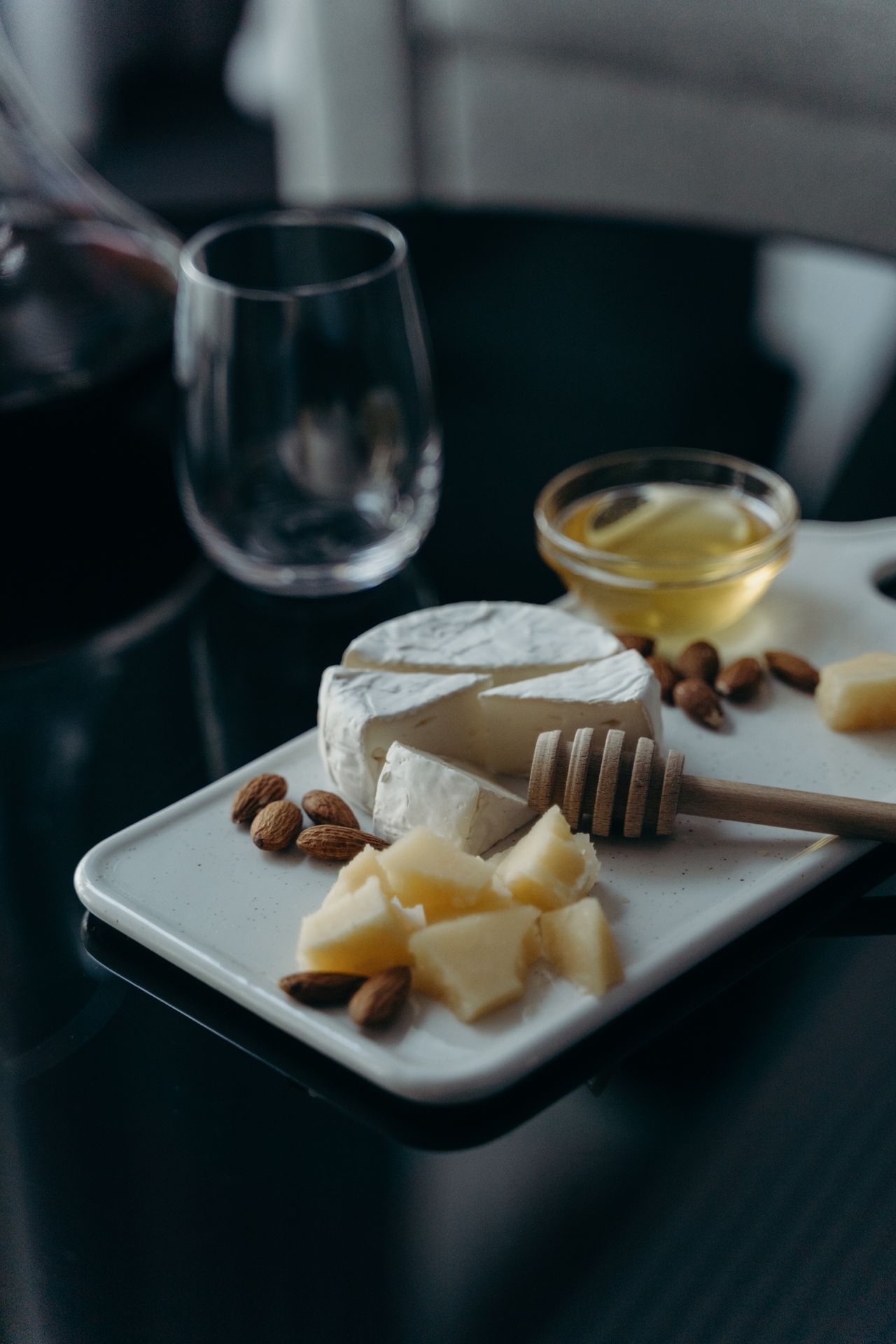Cheese, nuts, a bowl of honey and a wooden dipper sit on a white platter beside glasses.