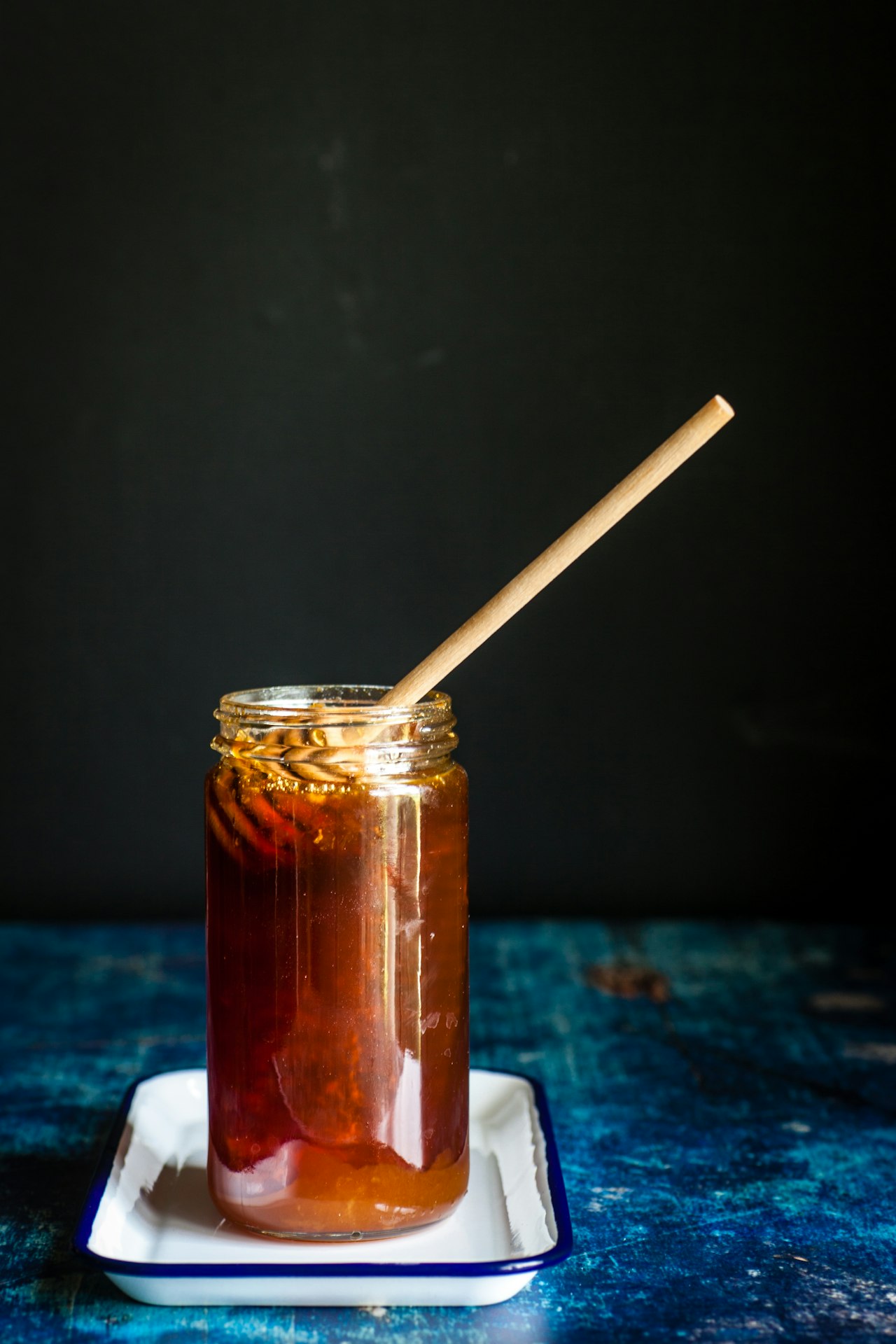 A glass jar of honey with a wooden utensil rests on a white tray.