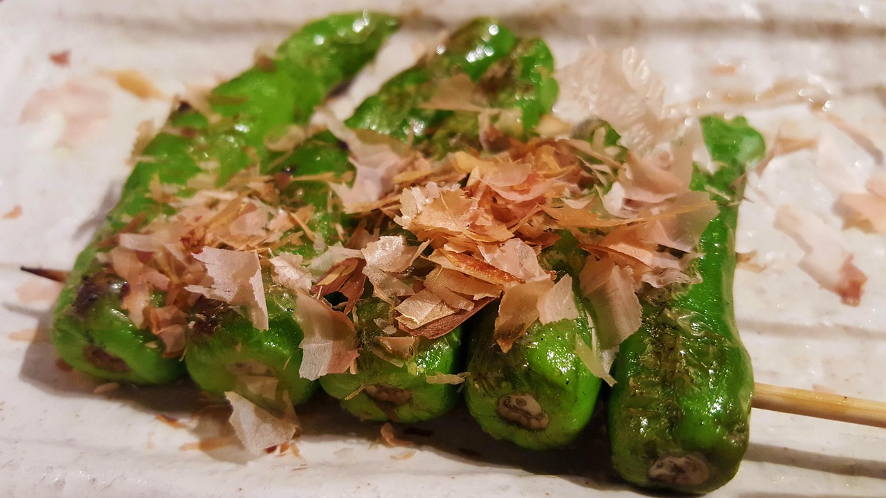 Cooked green peppers topped with thin pale flakes rest on a plate.