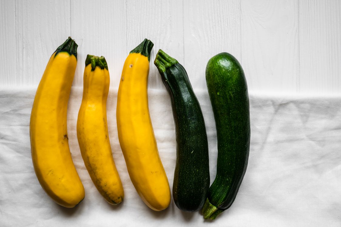 Yellow and green summer squash lie on white fabric.
