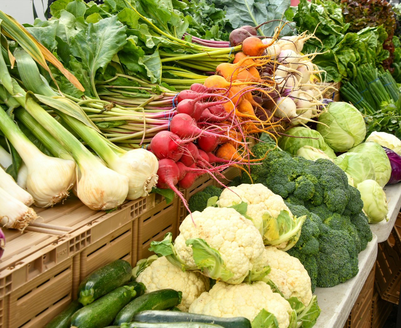 Mixed produce, including radishes, cauliflower and broccoli, fills a market stall.