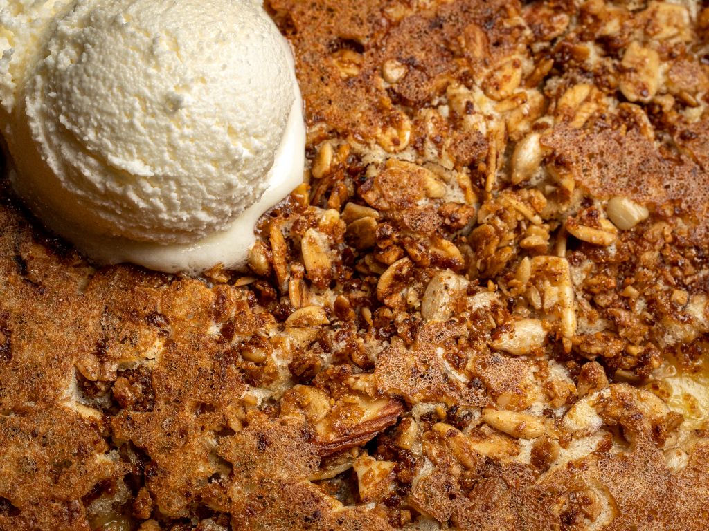 A scoop of pale ice cream on a baked dessert with nuts.