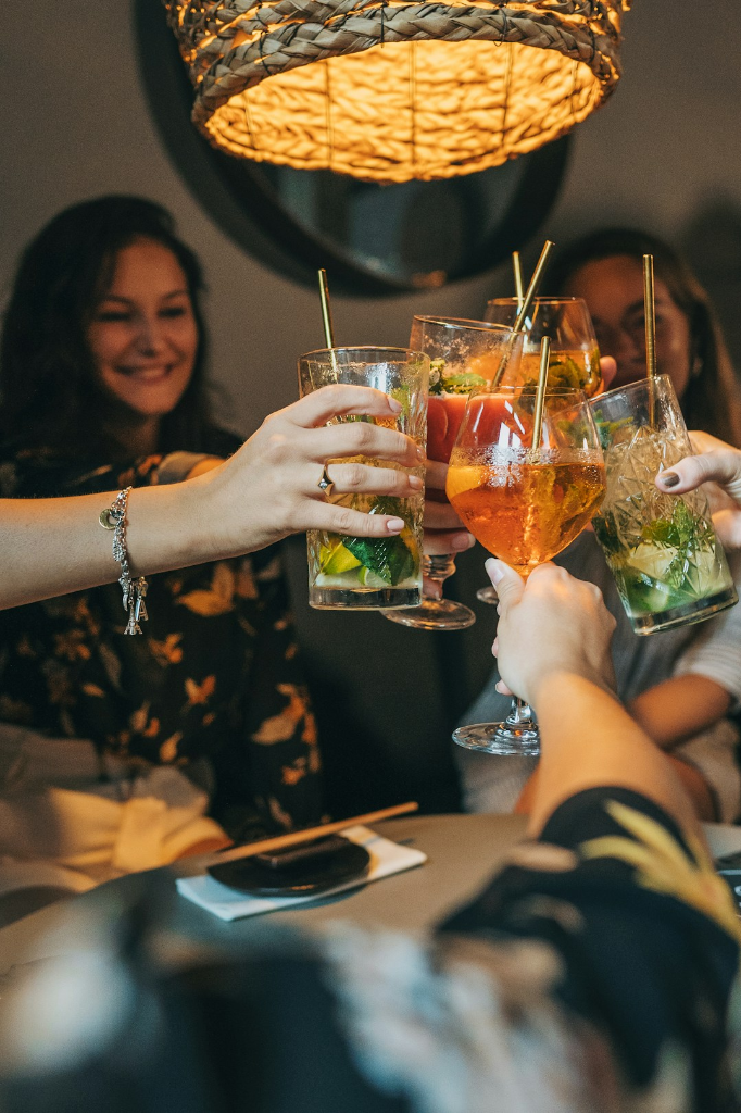 People raising several glasses of drinks at a table.