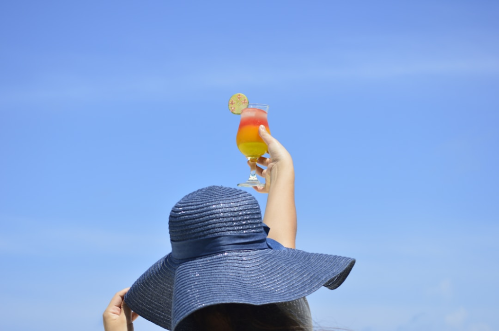 A person in a blue sun hat holding up a colorful drink outdoors.