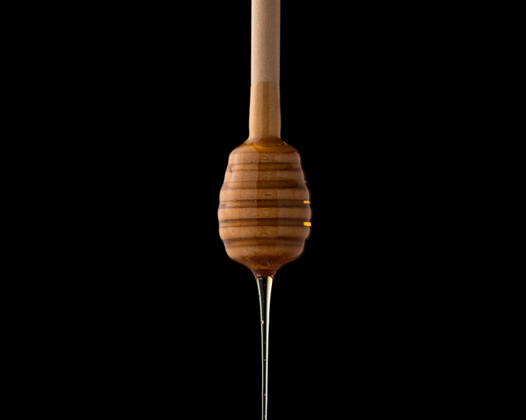 Honey dripping from a wooden dipper against a black background.