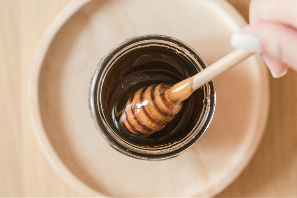 A wooden honey dipper in a glass jar on a round wooden plate.