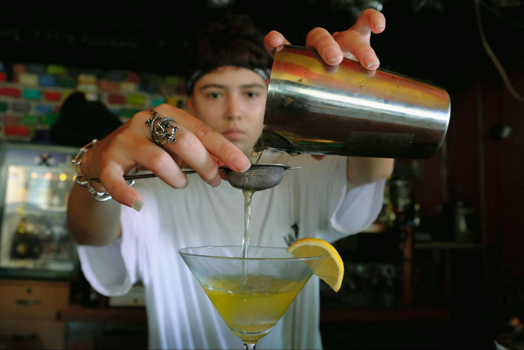 A bartender straining a drink into a glass with a citrus wedge.
