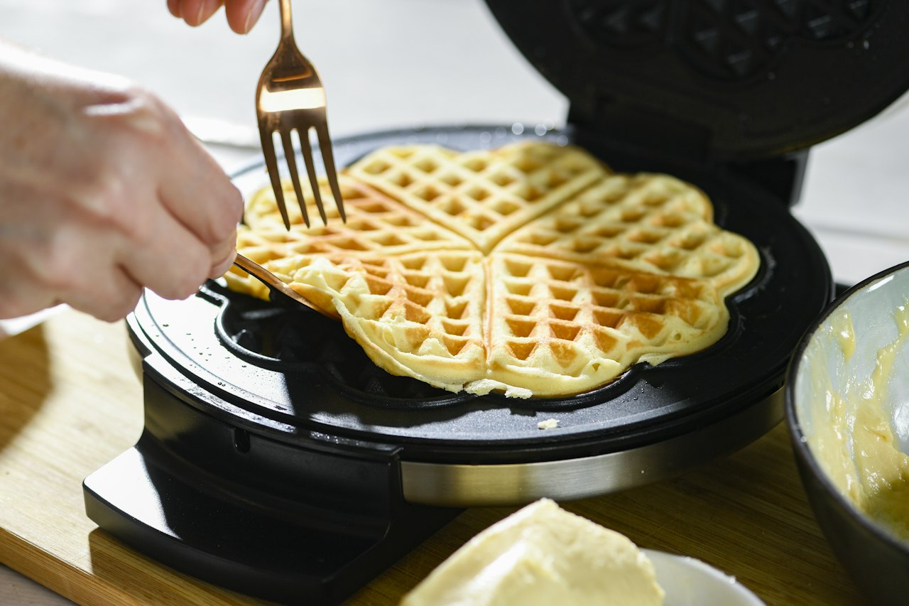 A fork lifts a heart-shaped waffle section from a round waffle maker.