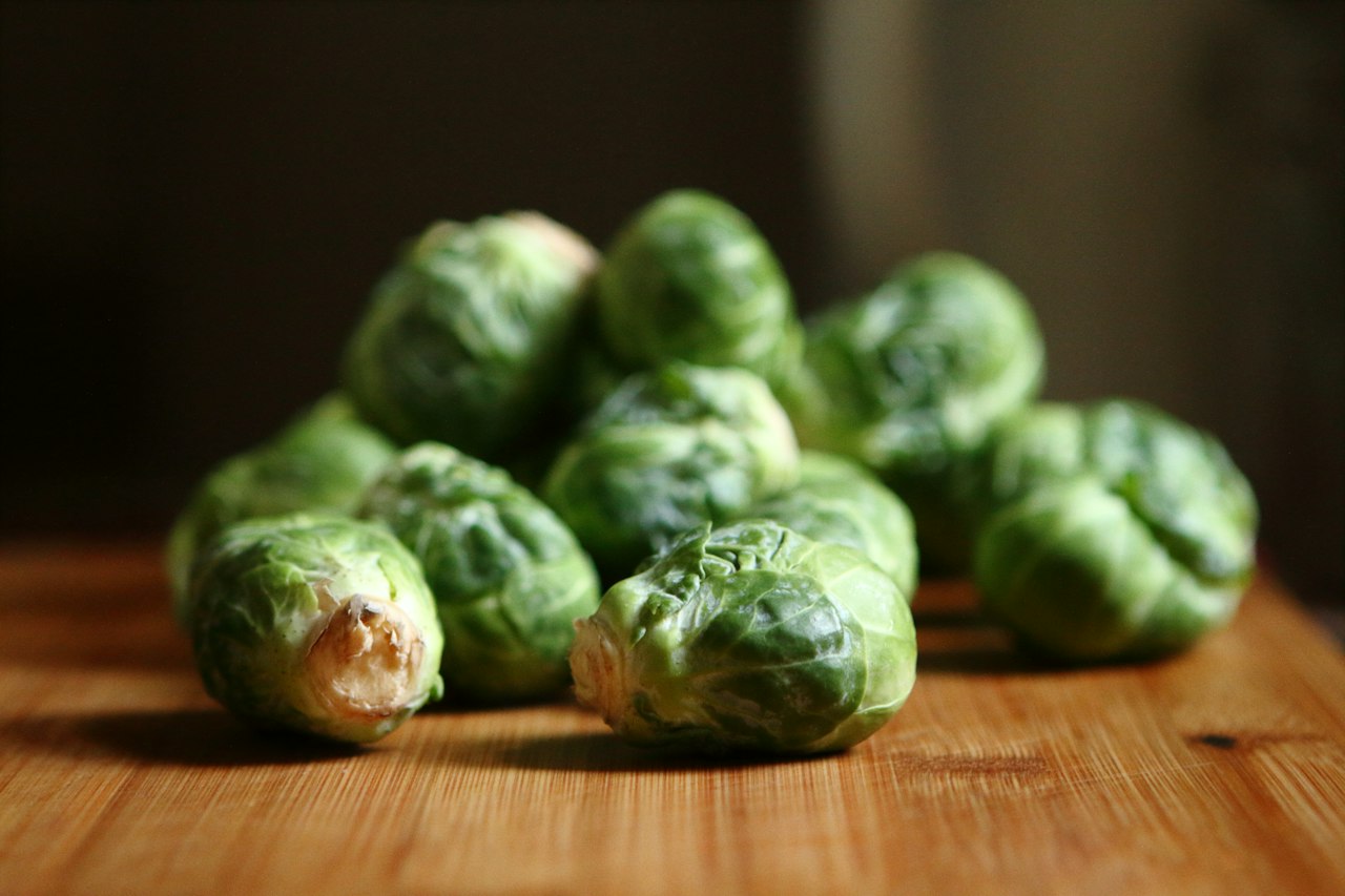 Raw Brussels sprouts sit on a wooden surface.